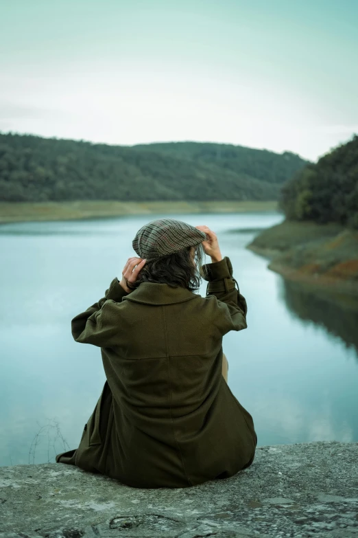 a woman sitting near the water is covering her face