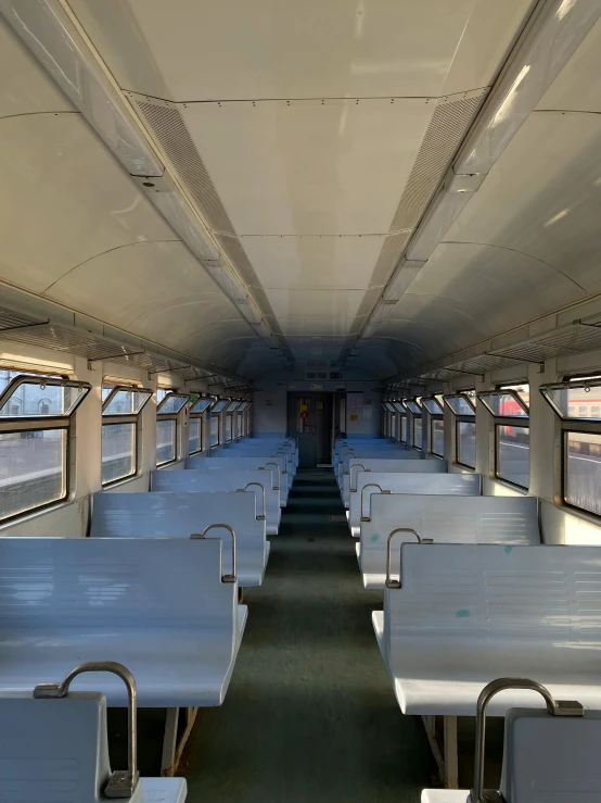 the inside of a commuter train car with many benches on one side and railings in front