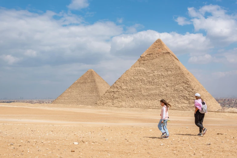 two people standing by a giraffe in front of three pyramids