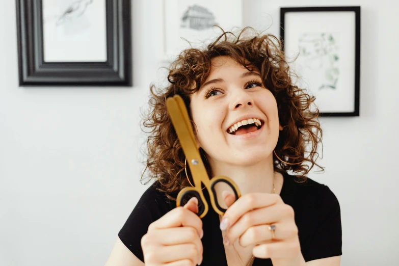 a woman with curly hair holding a pair of scissors up to her face