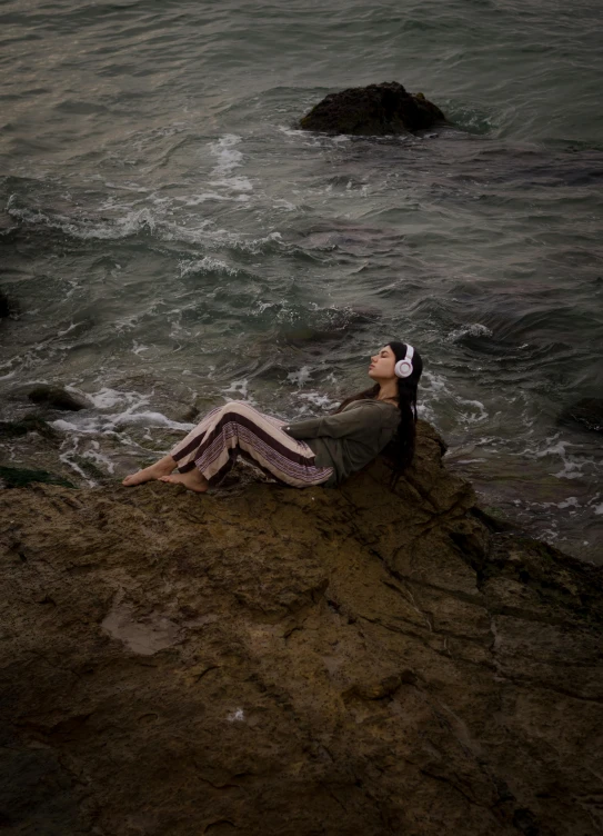 a woman laying on a rock in the water near the ocean