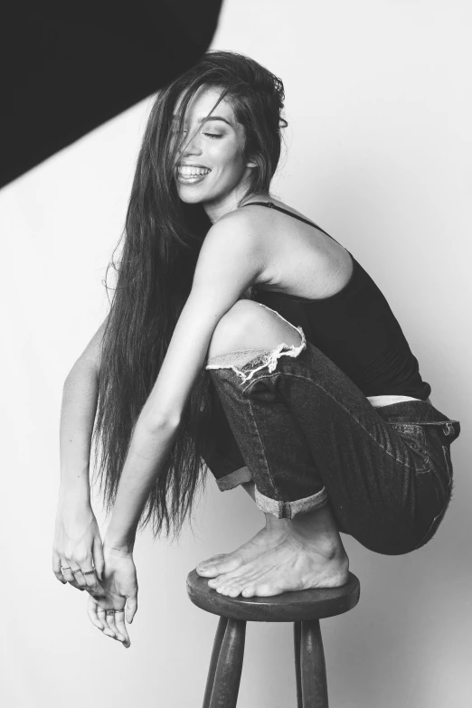 black and white pograph of smiling woman with long hair on stool