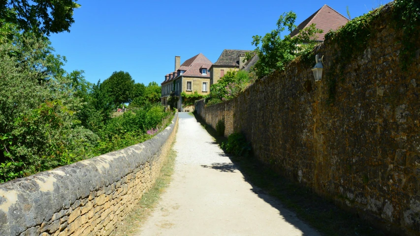 a road between a stone wall and house