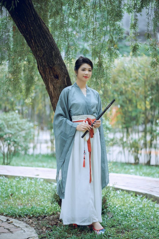 an asian woman in traditional clothing stands in front of the tree