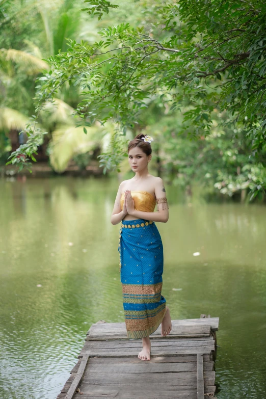 a young woman in a long dress standing on the edge of a lake with an apple