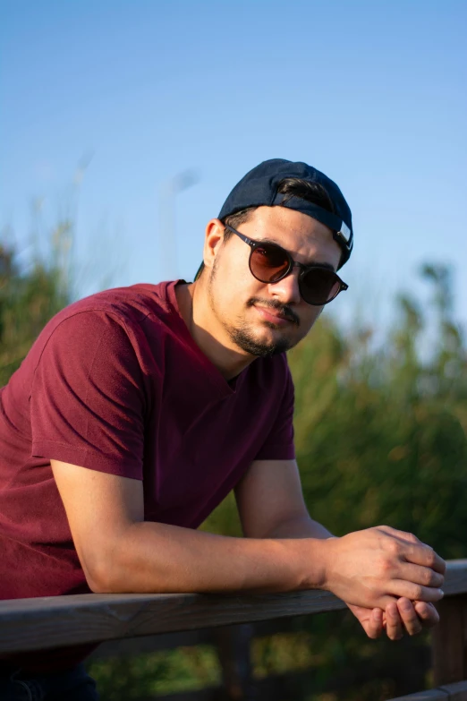 man wearing dark sunglasses and maroon shirt leaning on rail