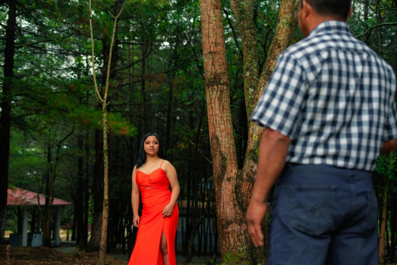 the woman in a red dress is standing near trees