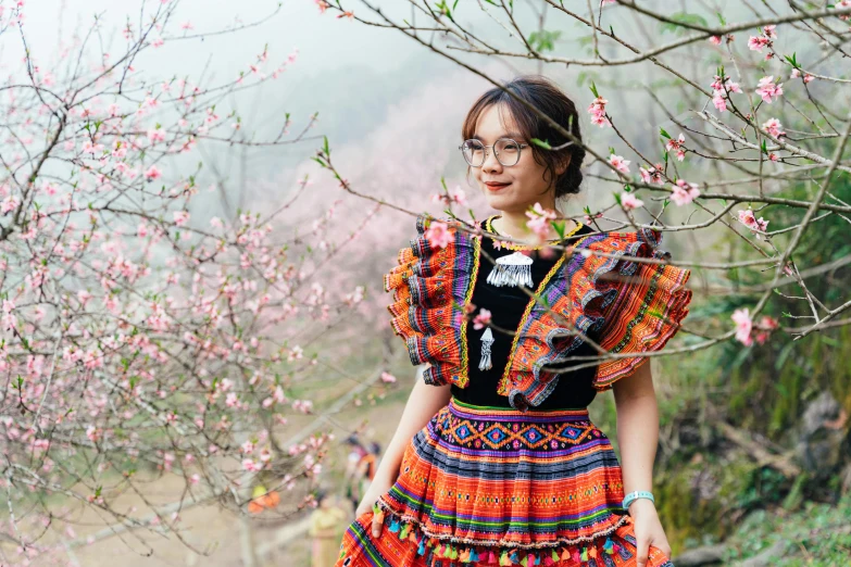 a woman with eye glasses stands next to a tree