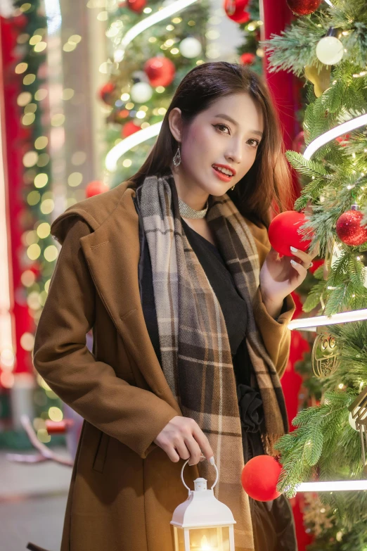 woman holding lantern in winter coat near large christmas tree