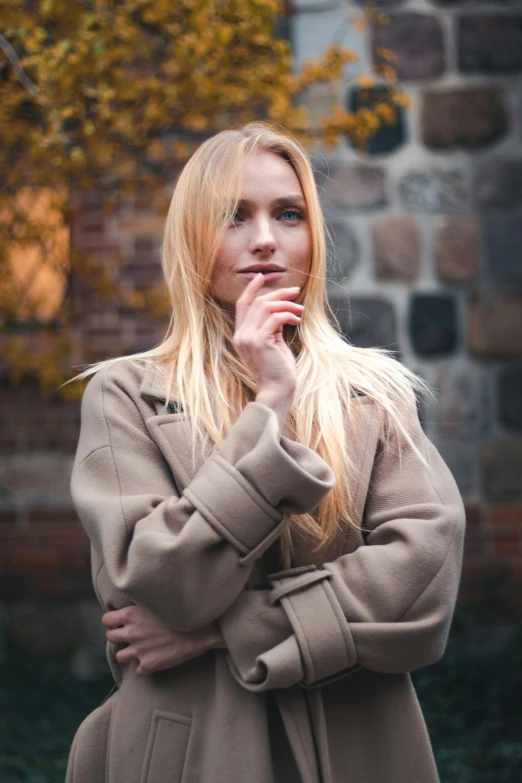 a blonde woman wearing a coat with her hand under her chin