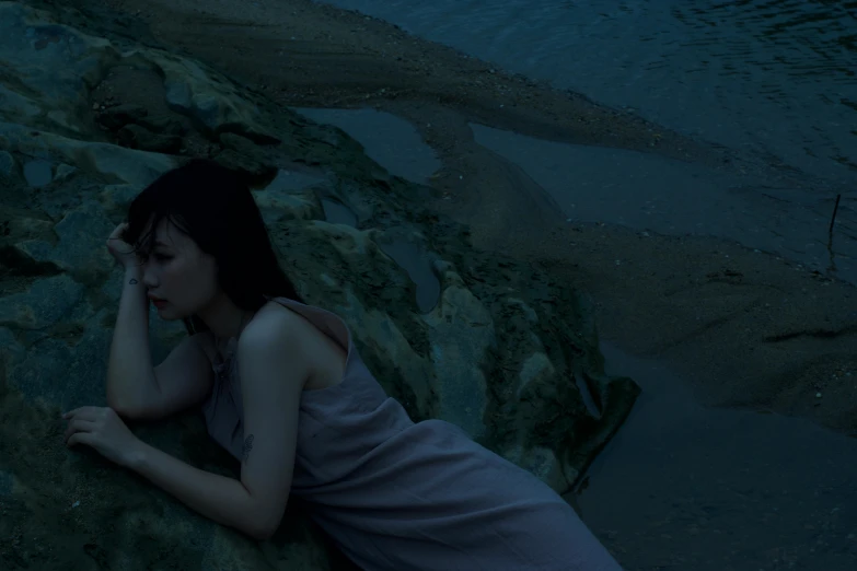 a young woman laying on top of a large rock near the ocean