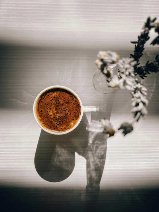 a coffee cup sitting on top of a white table next to a flower