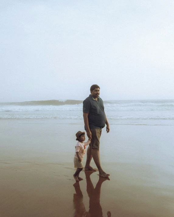 a man and small girl walking along a beach