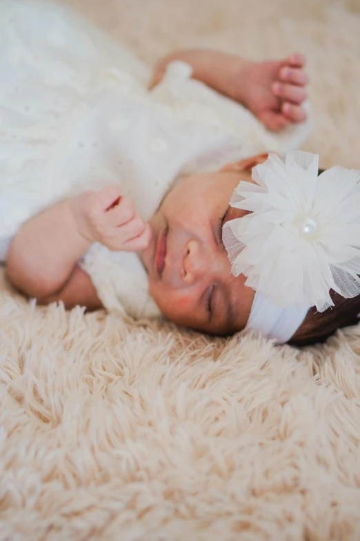 a newborn baby lying on her side with a white flower in its hair