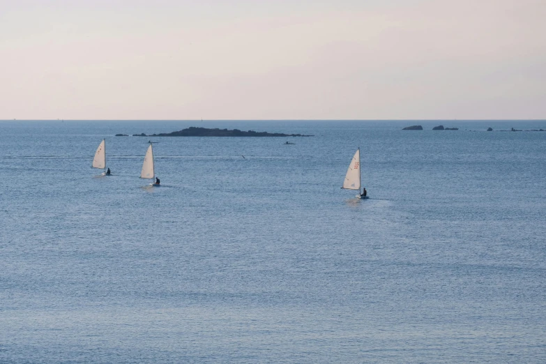 sailing dingks out on a beautiful ocean under a grey sky