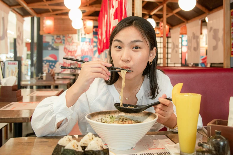 asian woman with chopsticks taking up bowl of noodles