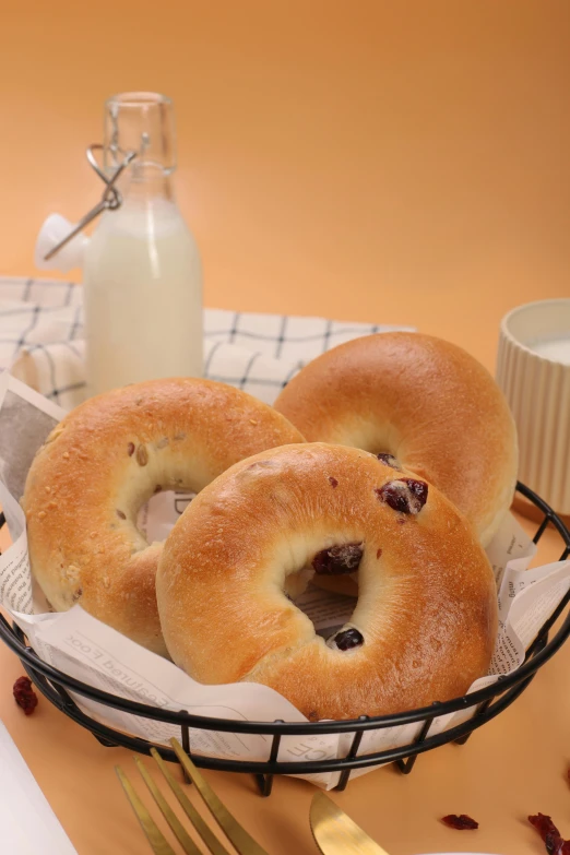 two blueberry bagels sit on a table with milk and dried berries