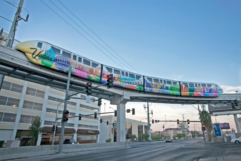 a multi - colored train passes over a street as traffic lights