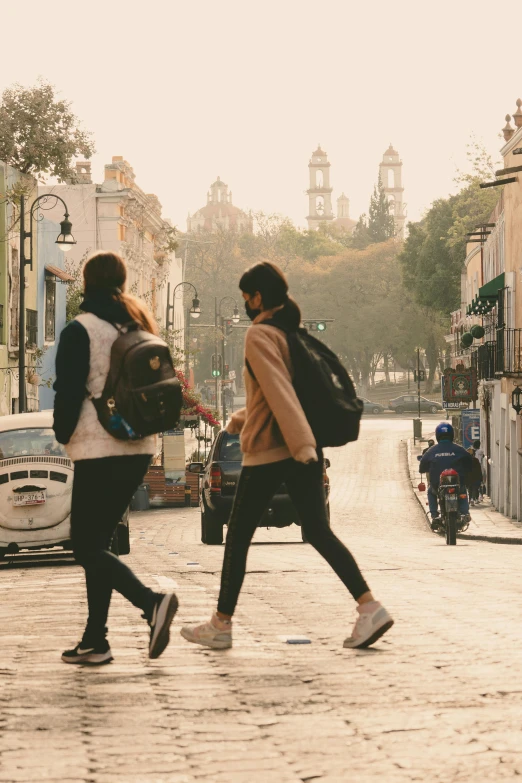 two women walking across the street with backpacks on