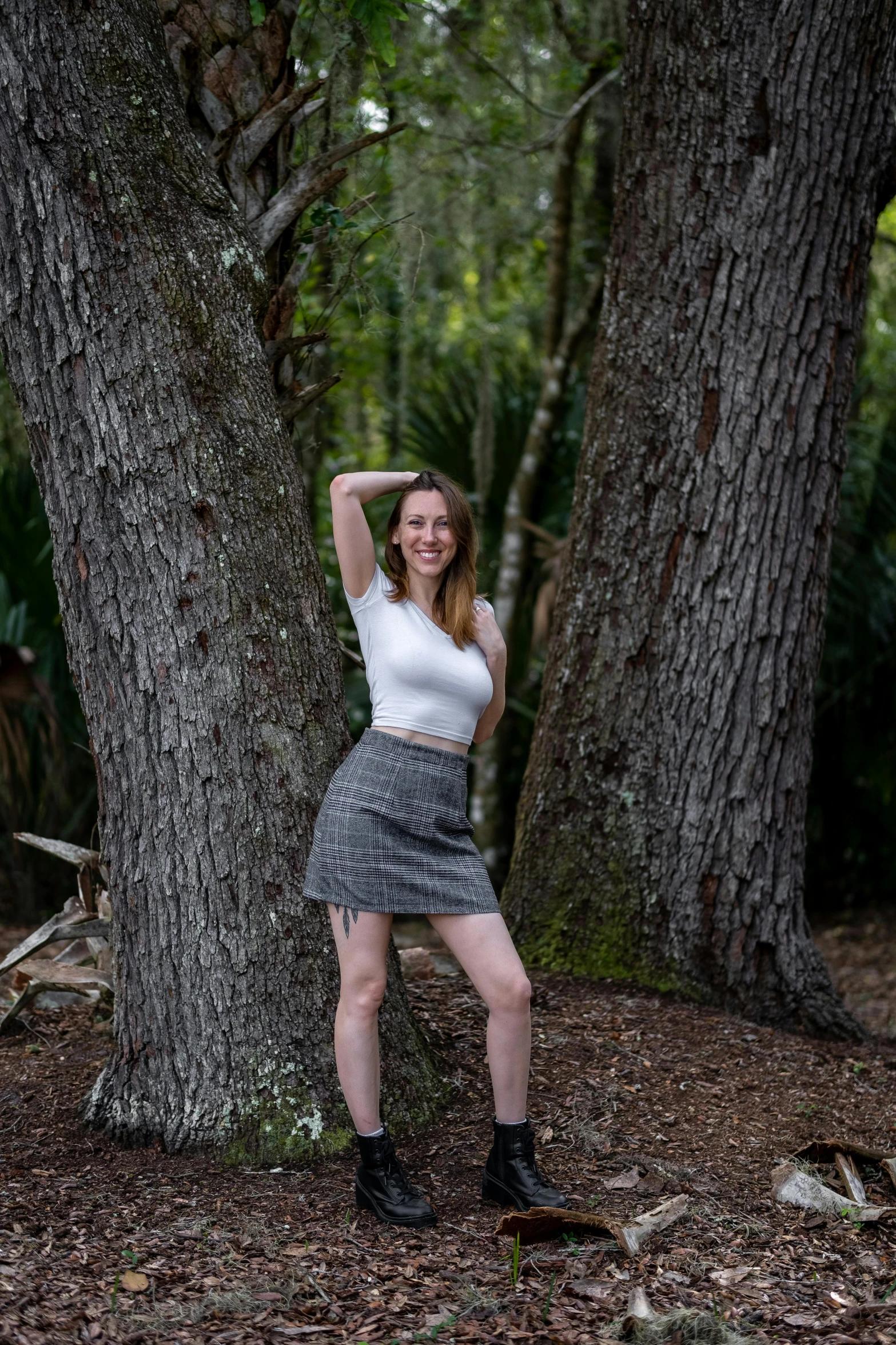 a smiling young woman leans against a tree