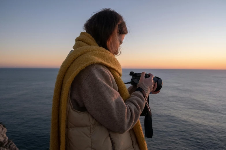 a woman holding a camera next to a body of water