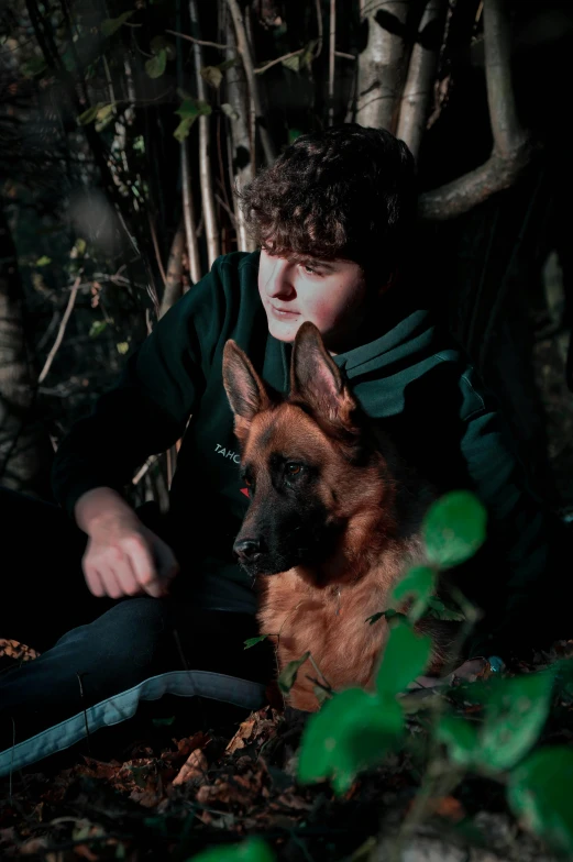 a young man is petting a dog outdoors in the woods