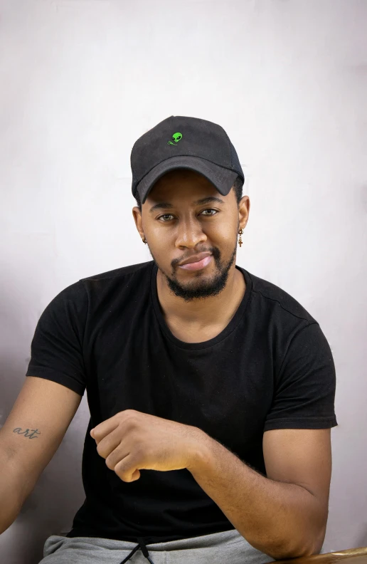 a young black man in a hat sitting next to a wooden table