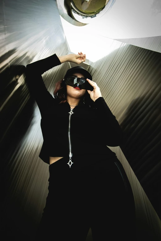 a woman wearing a black outfit and wearing sunglasses standing next to metal wall