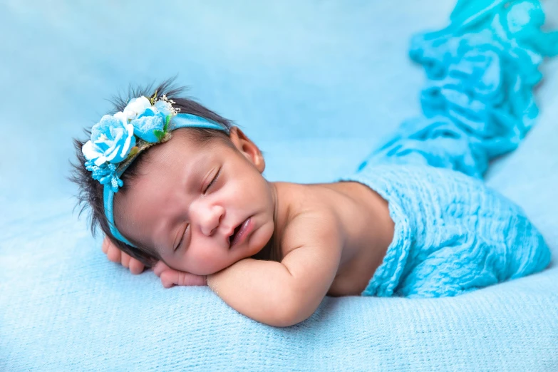 a sleeping newborn baby girl dressed in blue and a flower on her head