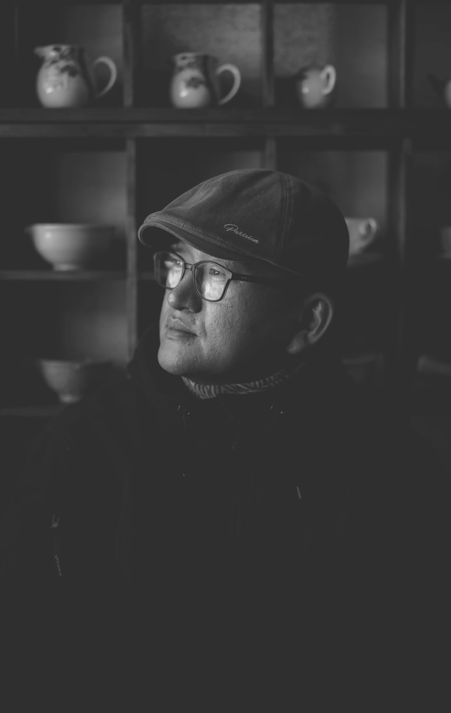 a man wearing glasses and a cap in front of shelves with cups