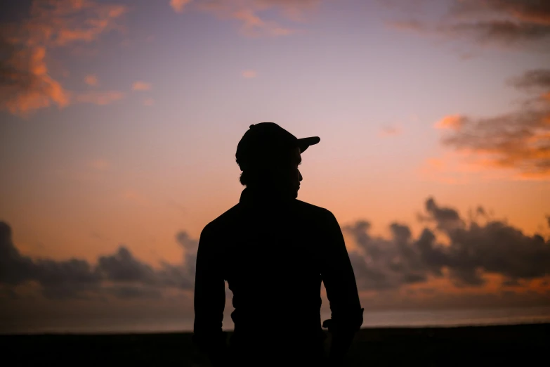 a silhouetted man wearing a hat looking towards the sunset