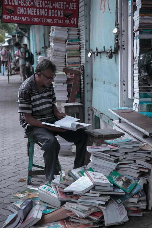 a man sits on a chair and looks at a pile of books