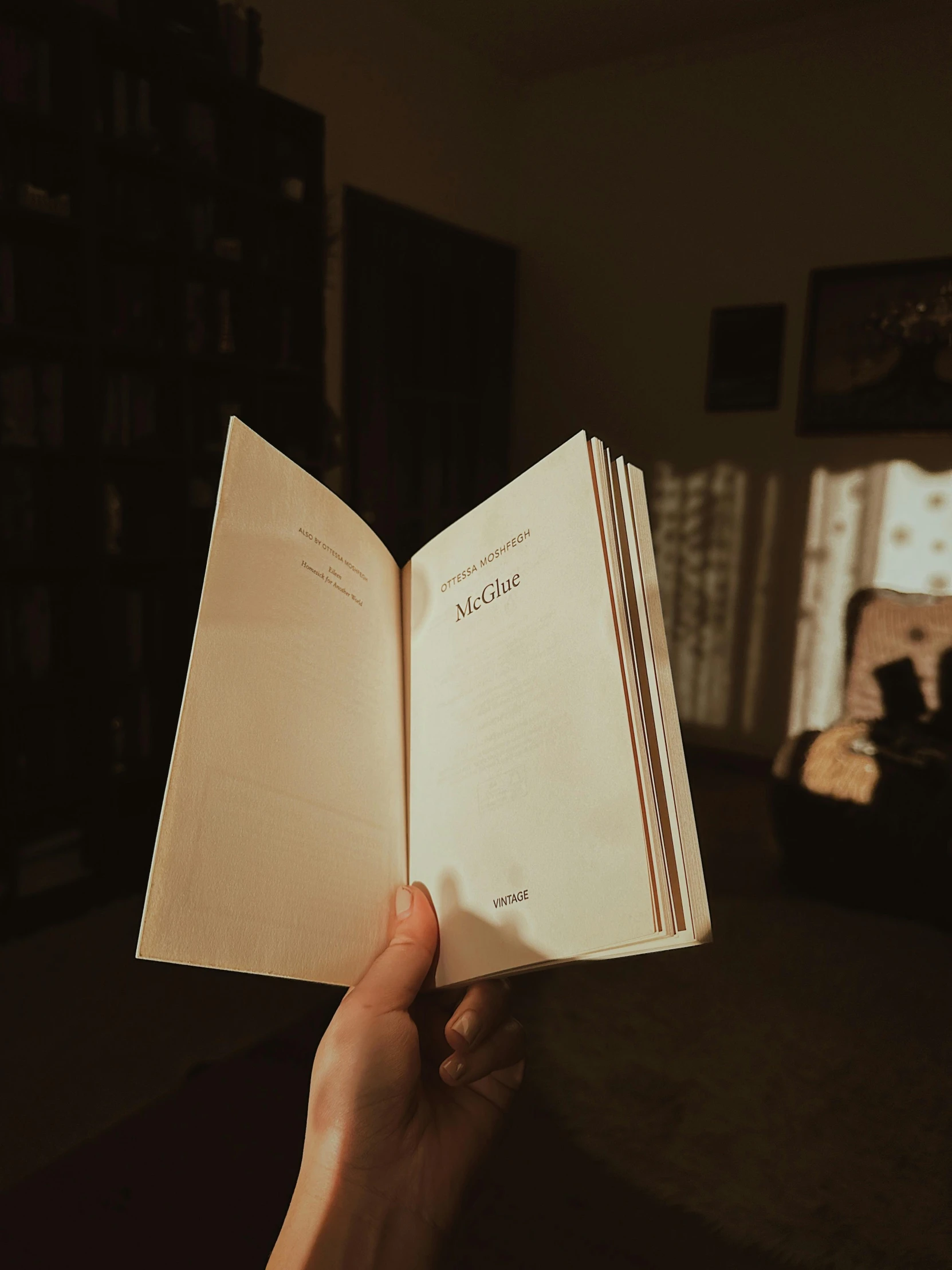 someone holding up an open book in front of a bookshelf