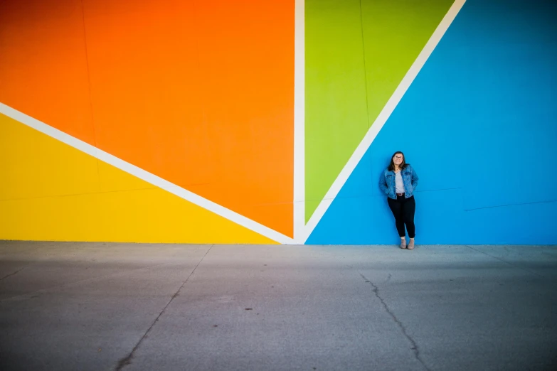 a woman standing against a wall in front of a colorful wall