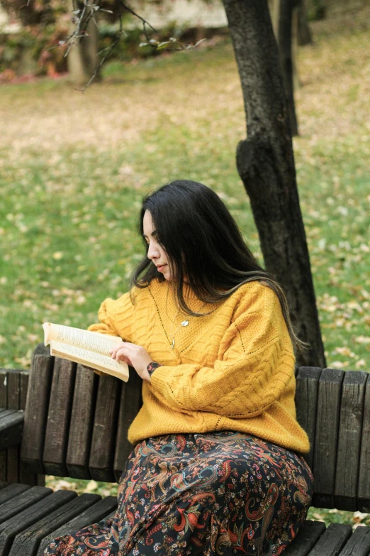 a girl sitting on a wooden bench reading a book