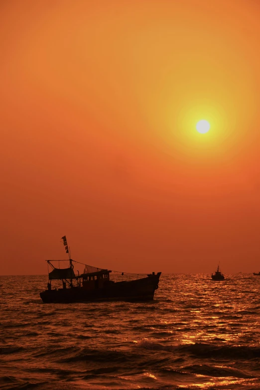 the sun sets over the ocean with two fishing boats in silhouette