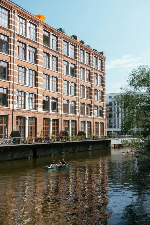 a rowboat travels along a river by a large brick building