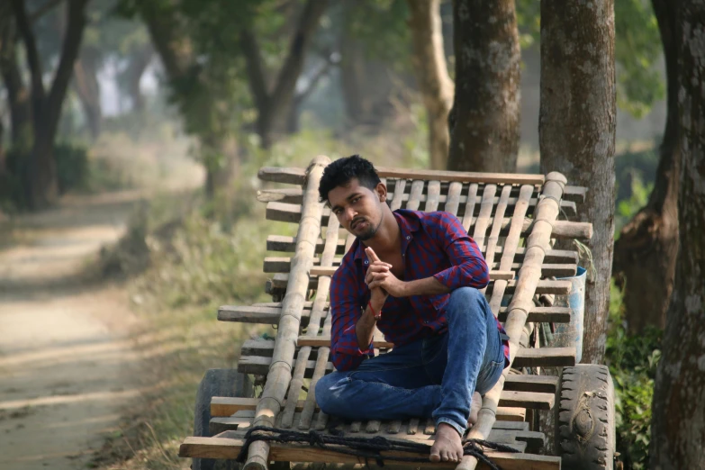 man sitting on bench made out of logs in the forest