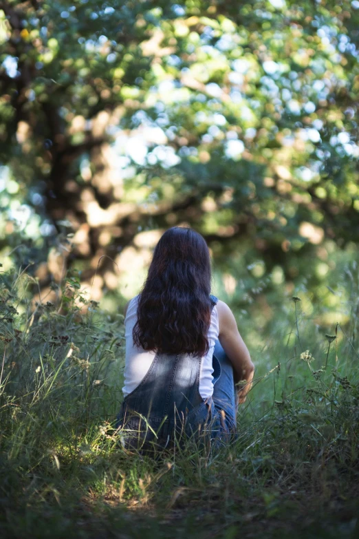 a woman sits in the grass under trees