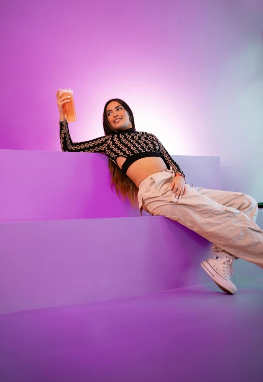 a woman is holding a beverage while lying on a wall