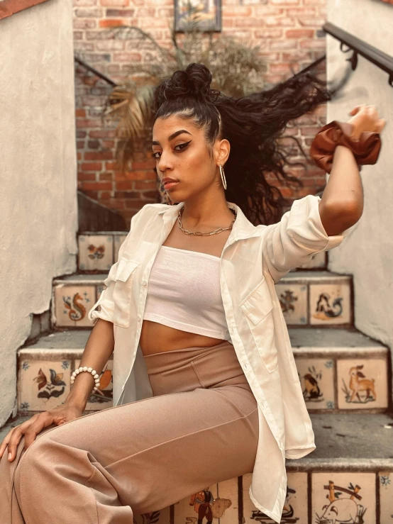 a young woman wearing a white shirt and brown pants sits on some stairs