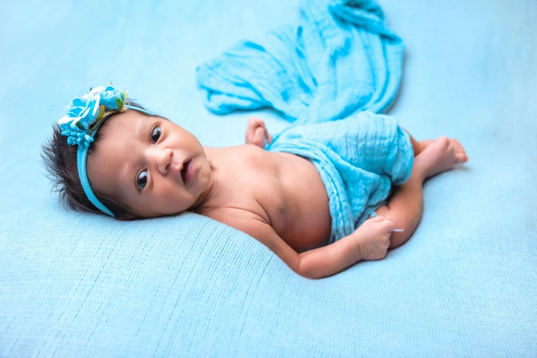 a baby with a blue bow lies on a blue sheet