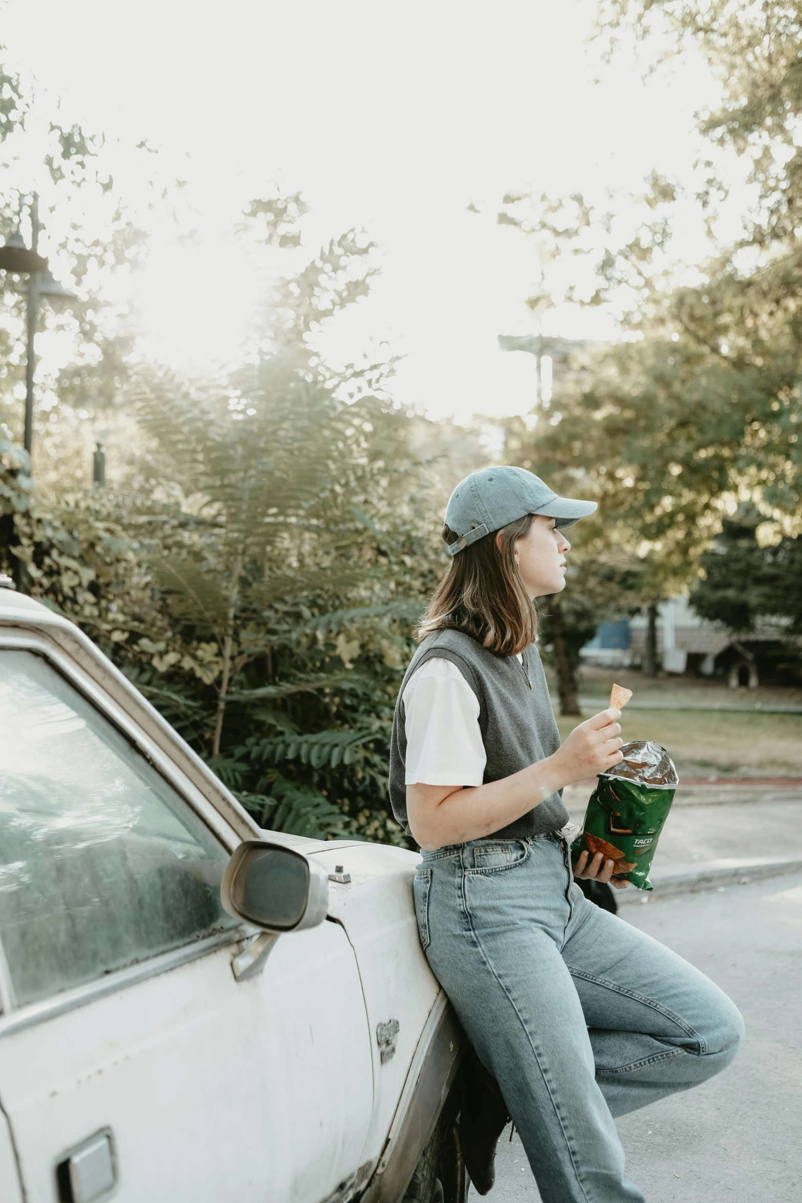 a girl sits on the back of an automobile with a soda in her hand