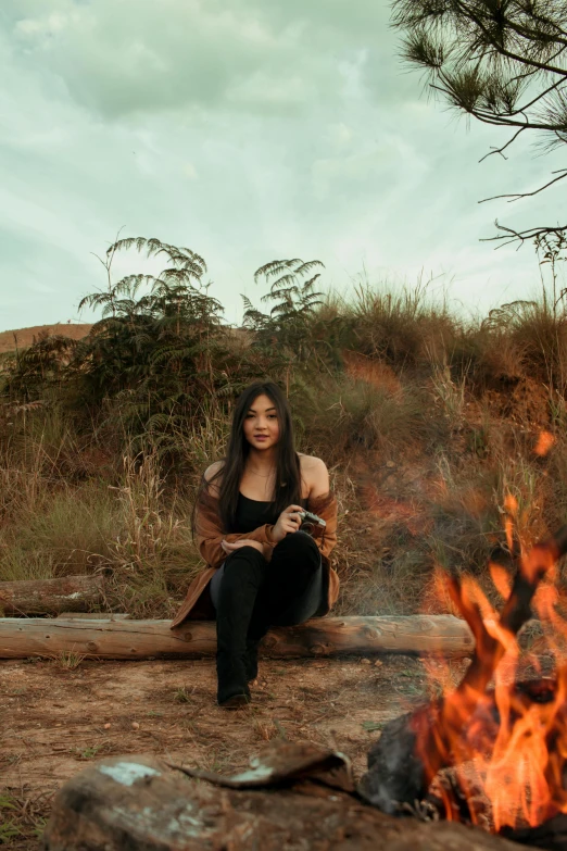 a beautiful young lady sitting in front of a fire while smoking a cigarette