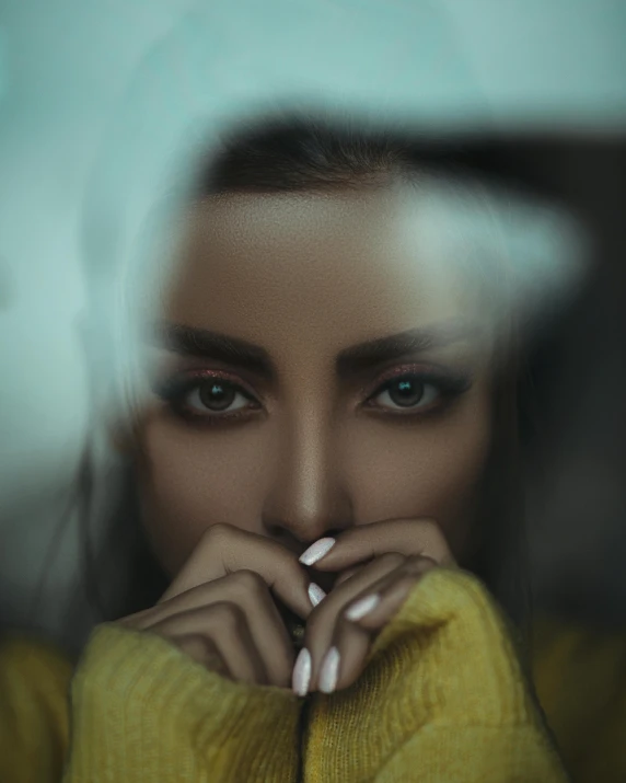 a woman is wearing a yellow sweater and holding her hands behind her face