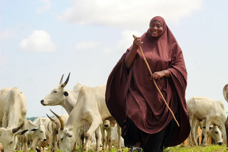 a woman walks with cattle in the background