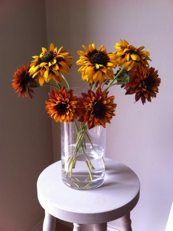 a white stool topped with a glass vase filled with flowers