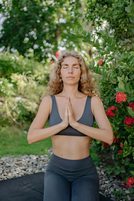 a beautiful woman in grey shirt and black yoga pants doing a meditation pose