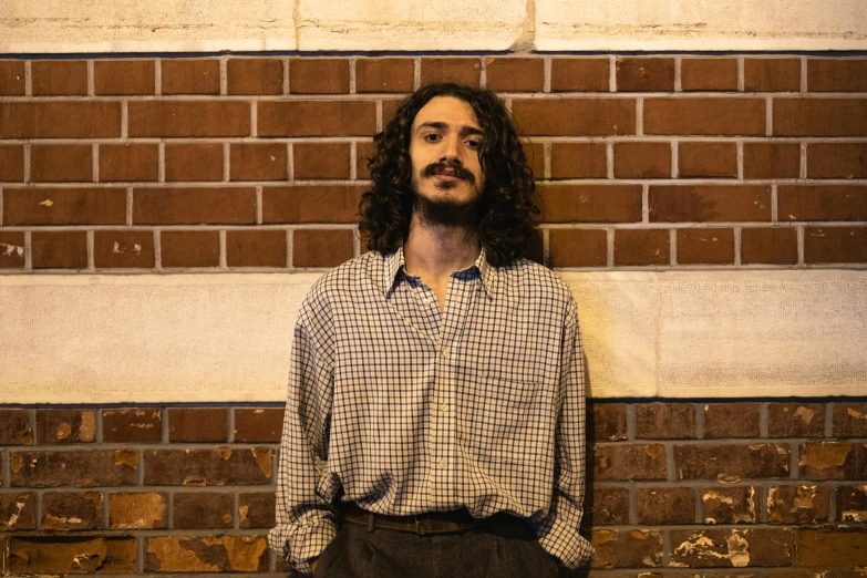 a bearded man standing against a brick wall