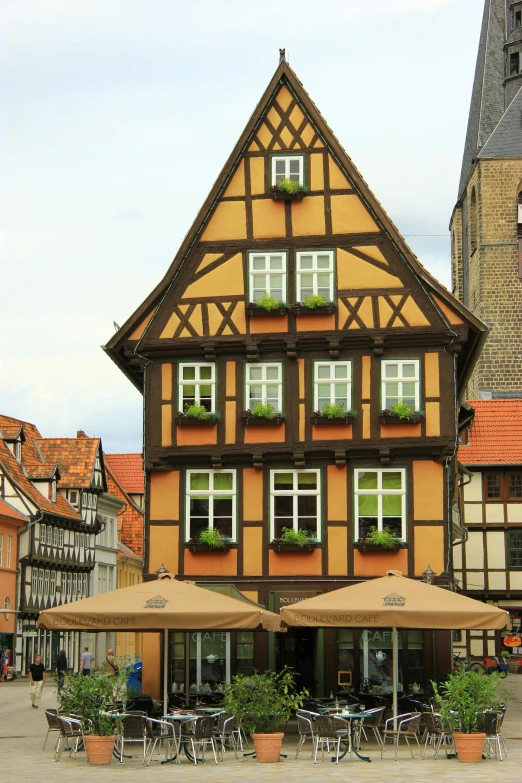 an old building in a town that has tables and chairs outside with umbrellas in front of the building